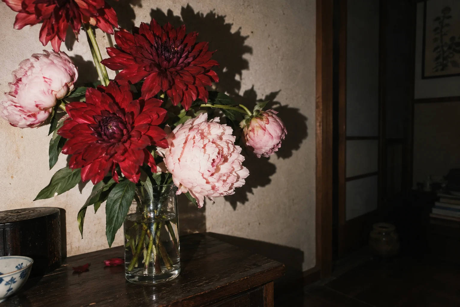 Red and pink flowers lit by direct flash in a dim, lived-in room.