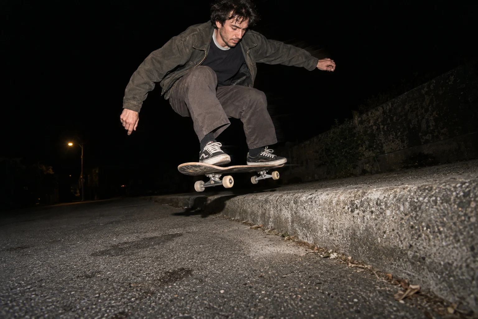 A skateboarder frozen above a curb by direct flash on a dark street.