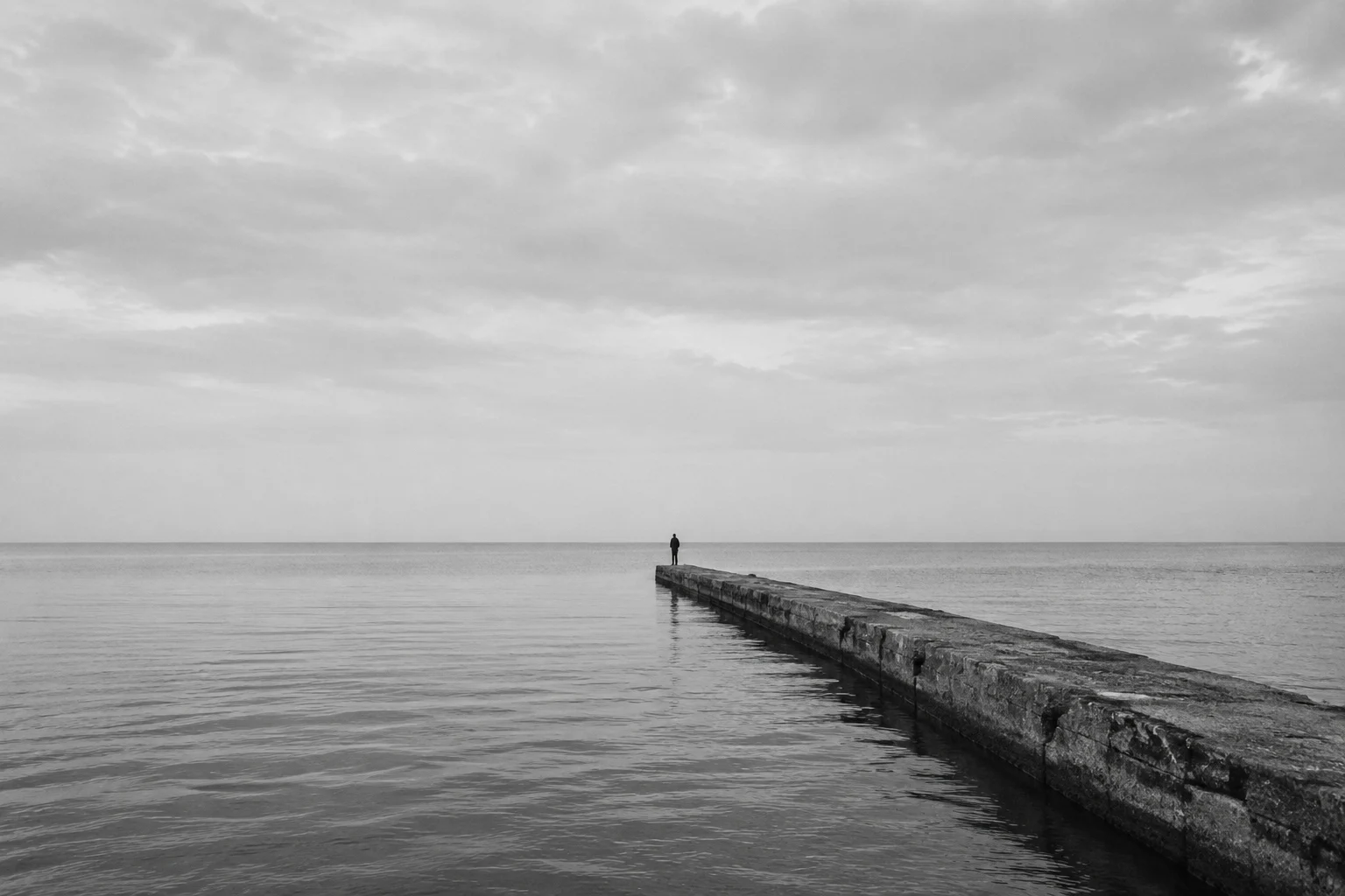 A quiet monochrome seascape with a low horizon and a solitary breakwater.